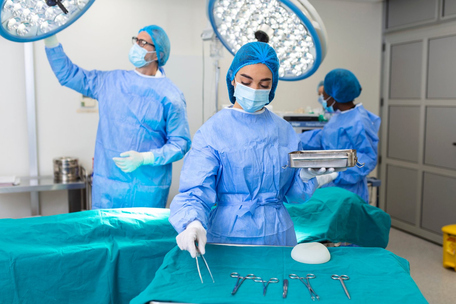 female surgeon in surgical uniform taking surgical instruments at operating room. young woman doctor in hospital operation theater